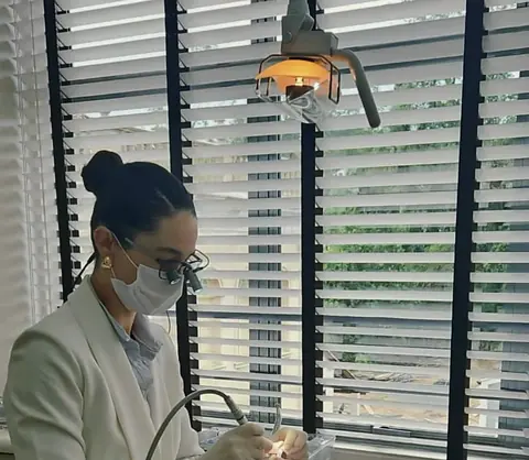 Dentista da equipe, de jaleco branco, atendendo um paciente na sala clara