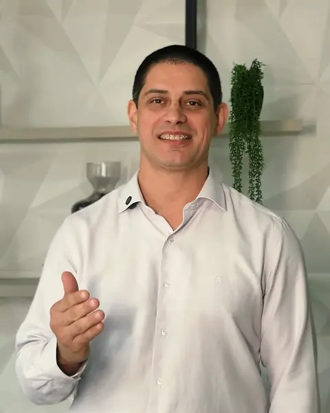 Dr. André Zavarise sorrindo, de camisa branca, no consultório